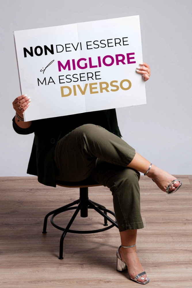 Simina seduta con un cartello che riporta la scritta non devi essere il migliore ma essere diverso